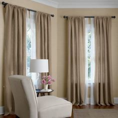 a chair and lamp in front of two windows with drapes on each side,