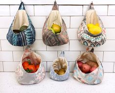 four bags hanging on the wall with fruits and vegetables in them, all lined up next to each other