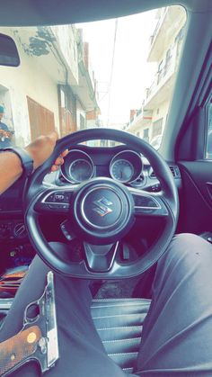 the interior of a small car with steering wheel and dashboard, in an urban setting