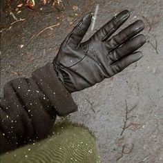 a person's hand wearing black gloves and holding something in their left hand with dirt on the ground