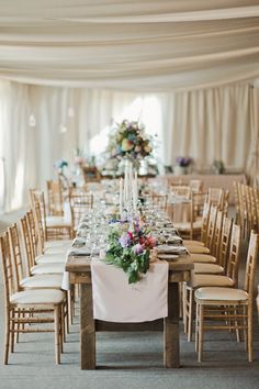 a long table set up with white linens and wooden chairs for an elegant wedding reception