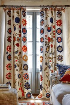 a living room filled with furniture next to a window covered in colorful curtains and pillows