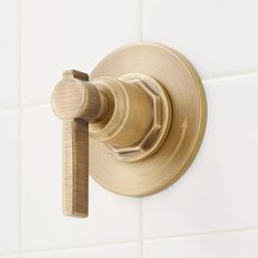 a brass shower faucet mounted on a white tile wall with a wooden handle