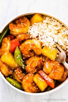 a bowl filled with chicken, pineapples, and rice next to a fork