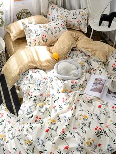 an unmade bed with yellow and red flowers on it, next to a window