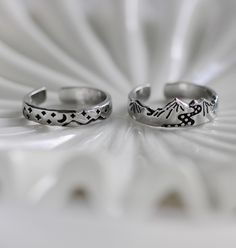 two silver rings sitting next to each other on top of a white surface with an intricate design