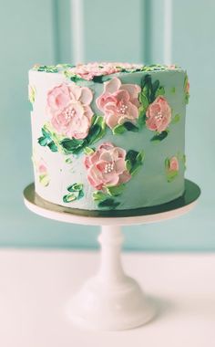 a blue cake with pink flowers on it sitting on a white pedestal in front of a turquoise wall