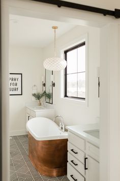 a bath tub sitting next to a bathroom sink under a window in a white room