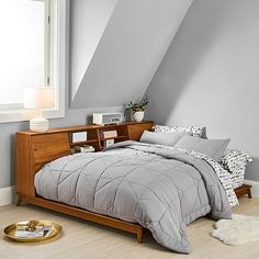 a bed sitting under a window next to a wooden dresser in a room with gray walls