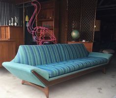 a blue couch sitting on top of a white floor next to a wooden shelf filled with vases