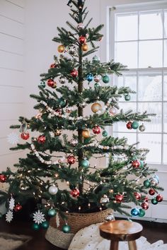 a small christmas tree with ornaments in a basket on the floor next to a window