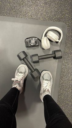 a pair of feet with headphones on top of a metal flooring mat next to a pair of black and white sneakers