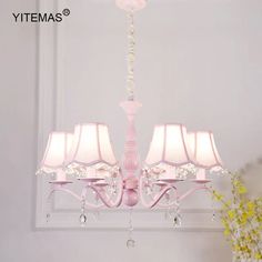 a pink chandelier with four lamps hanging from it's sides and flowers in the background