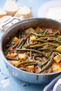 a pan filled with green beans and potatoes on top of a blue tablecloth next to bread