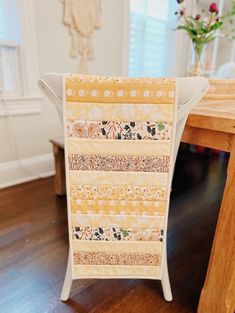 a wooden table topped with a white chair covered in patchwork quilted strips and flowers