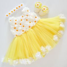 a yellow and white dress with flowers on the skirt, shoes and baby's booties