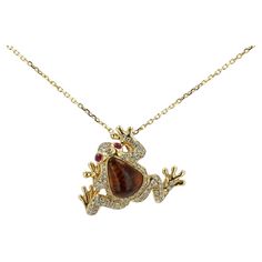 Representing renewal, prosperity and good fortune, this vibrant tree frog necklace is a fabulous gift for her. Centered by an abstract 3.22 carat earth colored tourmaline with glowing ruby eyes and a pavé diamond body, all displaying great attention to detail. A unique estate heirloom thoughtfully artisan-crafted of 18k yellow gold along with an 18" link chain. Photography © Bella Rosa Galleries Santa Barbara, CA Condition: Very Good Era: Contemporary Estate Year: 1980s Metal: 18k Yellow Gold Central Gemstone: Tourmaline: 3.22 Carats Accent Gemstones & Diamonds: 84 Round Brilliant Cuts 0.51 Carats Total 2 Cabochon Rubies 0.10 Carats Total Graded by GIA standards Dimensions: Length: 18" Pendant: 1" tall X 3/4" wide Weight: 8.1 grams Includes: Certified Appraisal upon request, custom box, & Chain Photography, Frog Necklace, Tree Frog, Good Fortune, Artisan Craft, Custom Boxes, Santa Barbara, Pave Diamonds, Link Chain