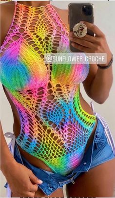 a woman wearing a colorful crochet top and denim shorts is taking a selfie with her cell phone