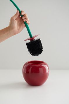 a hand holding a brush over a red vase with a black handle on the top