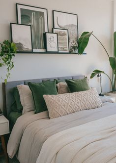 a bed with green pillows and pictures on the wall above it, in a bedroom