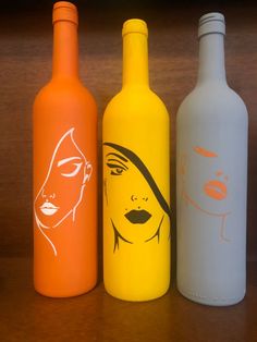 three different colored bottles sitting next to each other on a wooden table, one with a woman's face painted on it