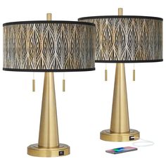 two gold table lamps with black and white fabric shades on them, one is plugged into the charger