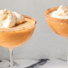 two glasses filled with drinks sitting on top of a marble counter topped with whipped cream