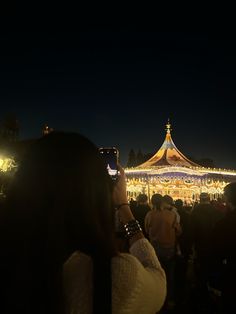 people are standing in front of a carousel at night with their cell phones up to their ears