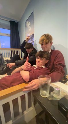 three young men sitting next to each other on top of a wooden bench in front of a window