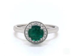 an oval emerald and diamond ring on a white background with the center stone surrounded by small diamonds