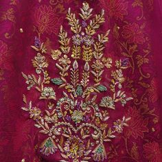 an embroidered red cloth with gold and green flowers on the side, in front of a pink background