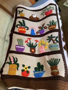 a crocheted blanket with potted plants and flowers on it, sitting on the floor