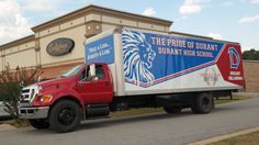 a red and white truck is parked in front of a building with the pride of durham logo on it