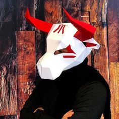 a man wearing a white mask with red horns on it's head and his arms crossed