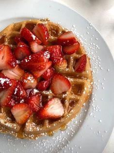 a waffle topped with strawberries and powdered sugar on a white platter