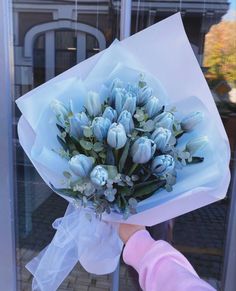 a person holding a bouquet of flowers in front of a glass door with a building behind it