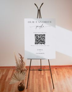 a white sign sitting on top of a wooden floor next to a potted plant