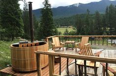 a wooden deck with chairs and an outdoor hot tub in the middle of it surrounded by mountains