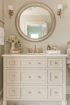 a bathroom with a large round mirror above the sink and white drawers on the counter