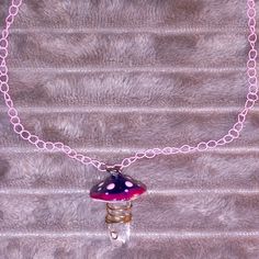 a pink and purple necklace with a small glass mushroom pendant hanging from it's chain