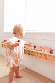 a toddler standing in front of a window looking at toys on the floor and shelf