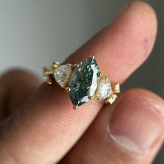 a close up of a person's hand holding an engagement ring with two pear shaped diamonds