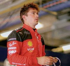 a man in a red and black racing suit holding a steering wheel while looking off to the side