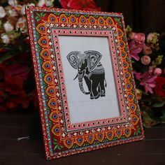 an elephant painted on the side of a wooden frame with flowers in the back ground