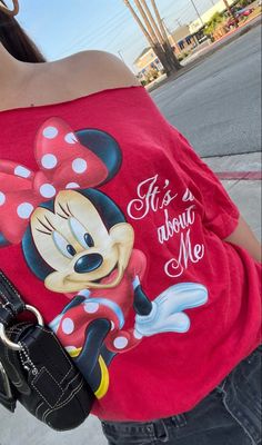 a woman wearing a minnie mouse shirt and carrying a black purse on her shoulder while walking down the street