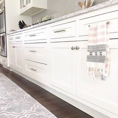 a kitchen with white cabinets and gray rugs on the hardwood flooring in front of it