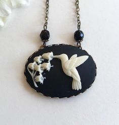 "Here is a super sweet hummingbird necklace featuring a nicely detailed cameo depicting a hummingbird with lily of the valley flowers. This cameo is black and white, it is horizontal style and set in an oxidized brass setting that is suspended from a nice quality non tarnish brass chain. You may select your desired chain length from the drop down menu. Handcrafted in the USA by Botanical Bird jewelry. Shipped in a lovely gift box and perfect for gift giving! Large Cameo Pendant measures: 1 1/4\" Hummingbird Jewelry, Black Cameo, Egyptian Necklace, Hummingbird Necklace, Lily Of The Valley Flowers, Hummingbird Pendant, Valley Flowers, Cameo Jewelry, Pretty Pendant