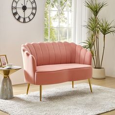 a pink couch sitting on top of a white rug next to a clock and potted plant