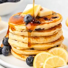 a stack of pancakes with syrup and blueberries on a plate next to sliced lemons