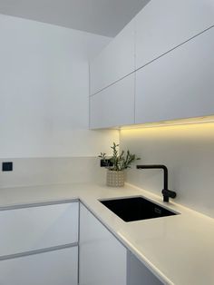 a white kitchen with a sink and black faucet next to the counter top